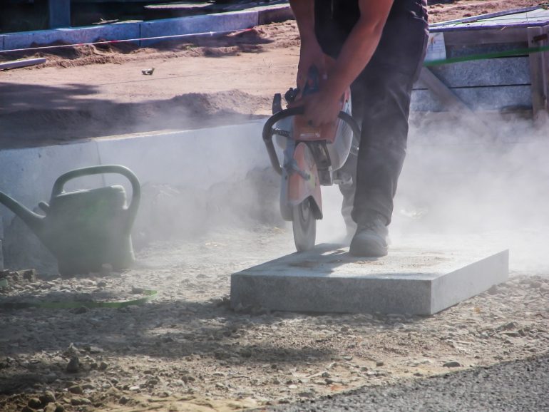 Construction worker using tool while dust blows into air - Construction dust