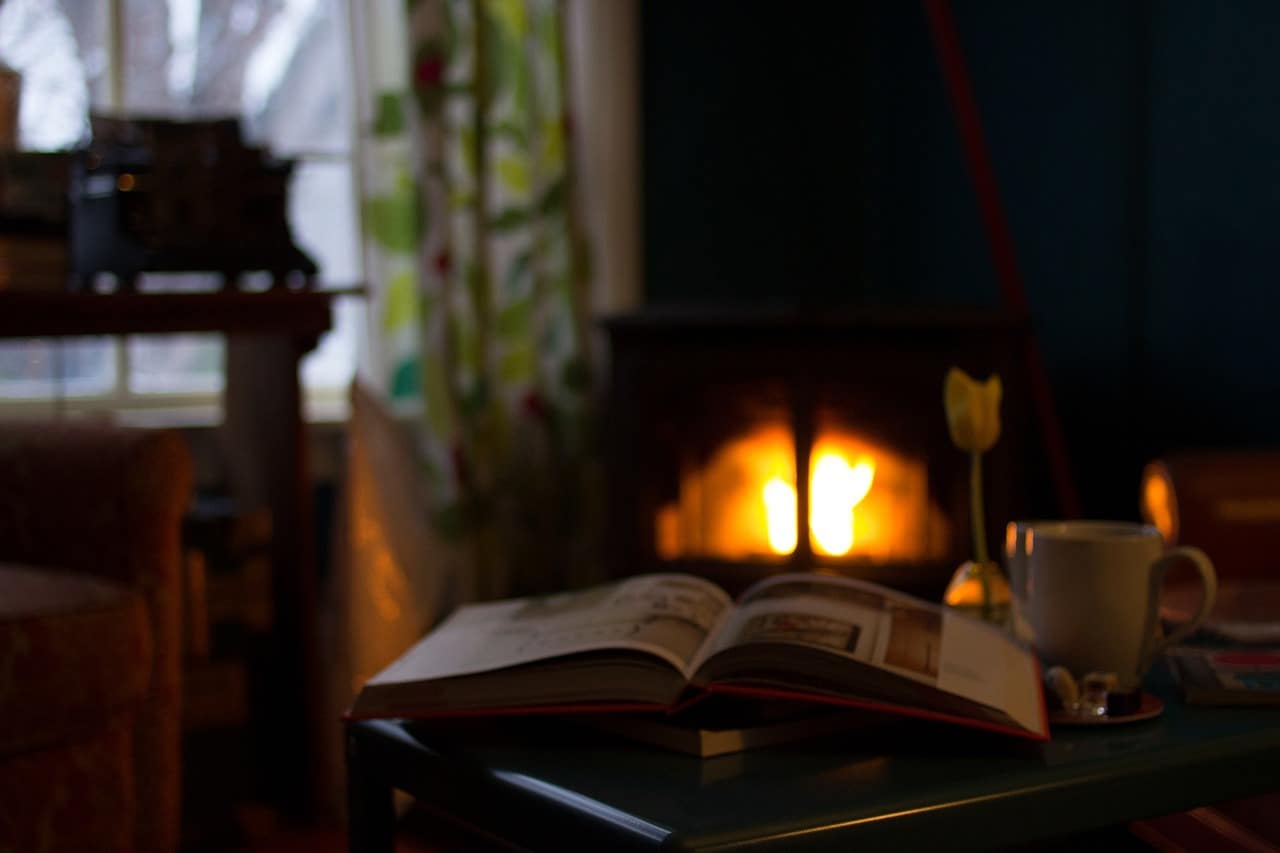 Book on table in front of fireplace beside window - 6 green strategies for reducing home heating costs