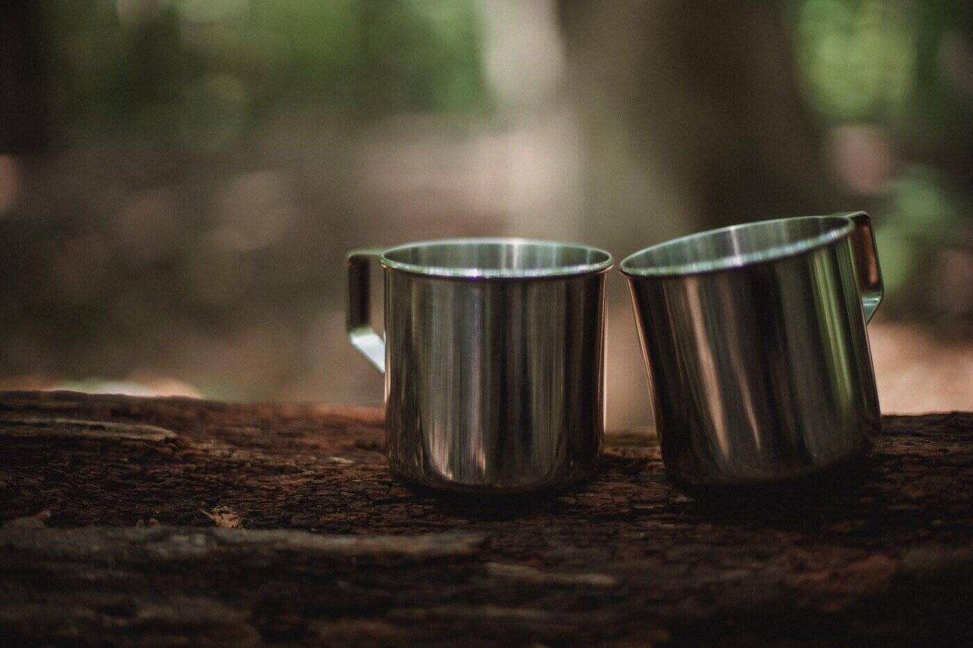 stainless steel cups on wooden table with forest background - tips for choosing eco-friendly cookware