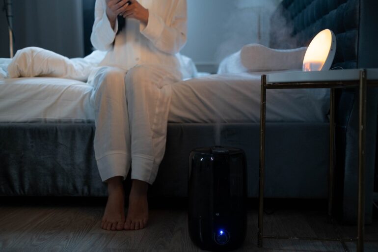 person in pyjamas sitting in bed with humidifier on floor - 5 best cool air and warm air humidifiers review