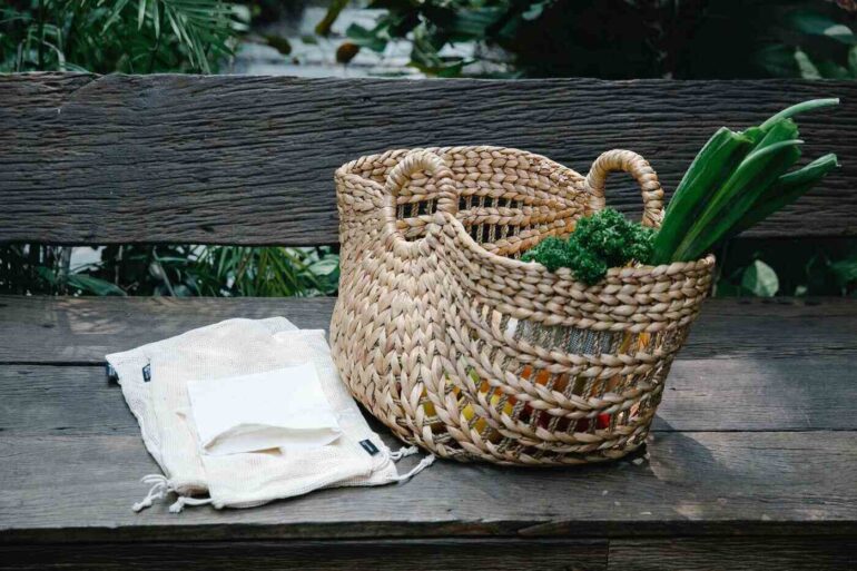 wicker grocery basket on bench with reusable bags - turning your home zero-waste in 7 easy steps